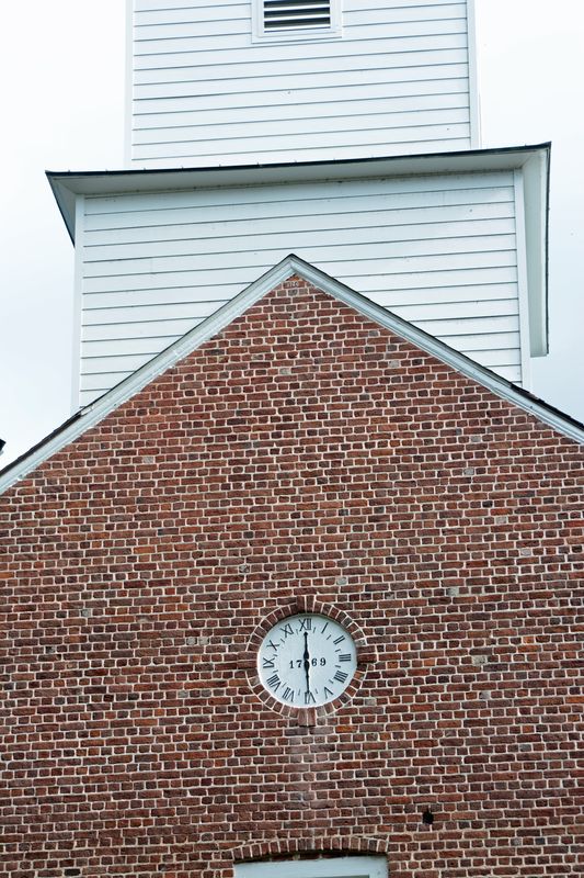 Clock face set in the brick gable just below the white wooden steeple