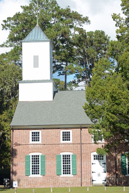 The white steeple rising above the brick church and green trees